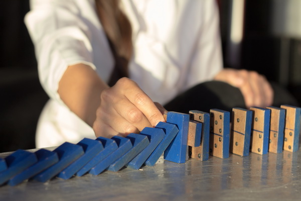 businesswomen hand Stopping Falling wooden Dominoes effect from continuous toppled or risk, strategy and successful intervention concept for business.